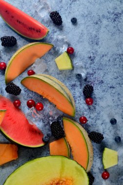 Taze kesilmiş kavun, karpuz, böğürtlen ve buz küpleri mavi taştan arka planda. Boşluk ve metin alanını kopyala