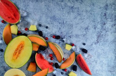Taze kesilmiş kavun, karpuz, böğürtlen ve buz küpleri mavi taştan arka planda. Boşluk ve metin alanını kopyala