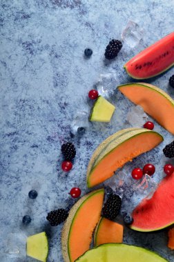 Taze kesilmiş kavun, karpuz, böğürtlen ve buz küpleri mavi taştan arka planda. Boşluk ve metin alanını kopyala