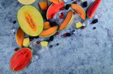 Taze kesilmiş kavun, karpuz, böğürtlen ve buz küpleri mavi taştan arka planda. Boşluk ve metin alanını kopyala