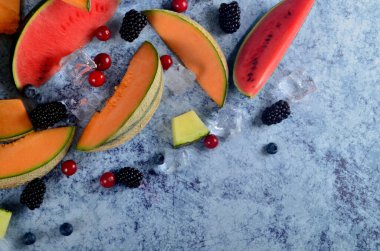 Taze kesilmiş kavun, karpuz, böğürtlen ve buz küpleri mavi taştan arka planda. Boşluk ve metin alanını kopyala