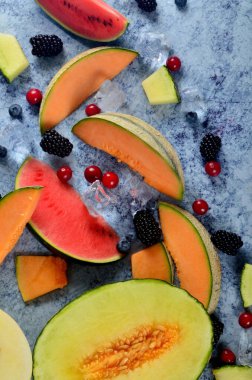 Taze kesilmiş kavun, karpuz, böğürtlen ve buz küpleri mavi taştan arka planda. Boşluk ve metin alanını kopyala