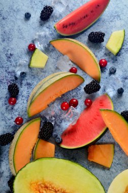 Taze kesilmiş kavun, karpuz, böğürtlen ve buz küpleri mavi taştan arka planda. Boşluk ve metin alanını kopyala