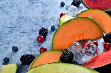 Taze kesilmiş kavun, karpuz, böğürtlen ve buz küpleri mavi taştan arka planda. Boşluk ve metin alanını kopyala