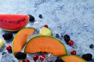 Taze kesilmiş kavun, karpuz, böğürtlen ve buz küpleri mavi taştan arka planda. Boşluk ve metin alanını kopyala