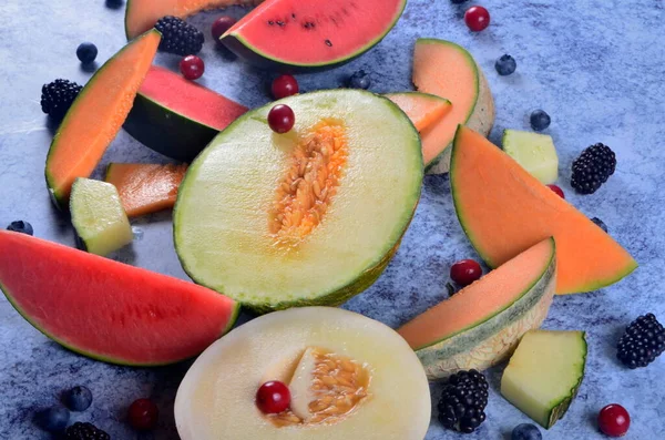 Taze kesilmiş kavunlar, karpuz ve böğürtlenler mavi taştan bir arka planda. 