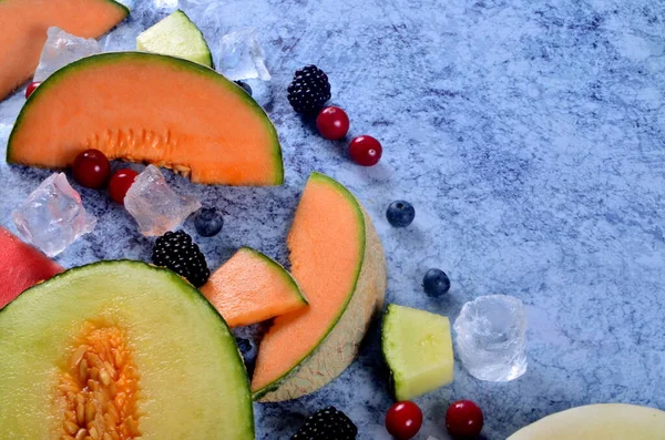 Taze kesilmiş kavun, karpuz, böğürtlen ve buz küpleri mavi taştan arka planda. Boşluk ve metin alanını kopyala