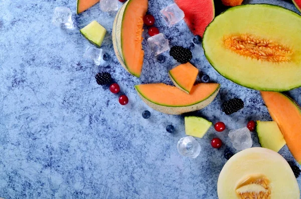 Taze kesilmiş kavun, karpuz, böğürtlen ve buz küpleri mavi taştan arka planda. Boşluk ve metin alanını kopyala