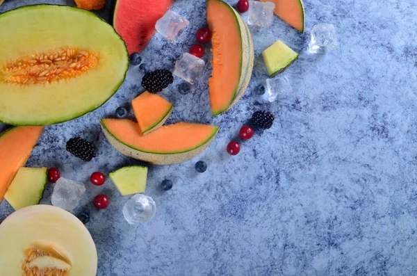Taze kesilmiş kavun, karpuz, böğürtlen ve buz küpleri mavi taştan arka planda. Boşluk ve metin alanını kopyala