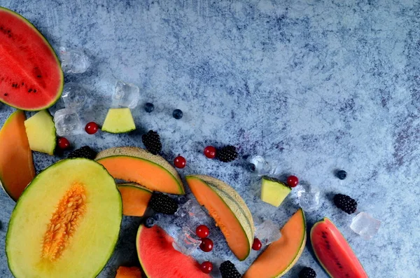 Taze kesilmiş kavun, karpuz, böğürtlen ve buz küpleri mavi taştan arka planda. Boşluk ve metin alanını kopyala