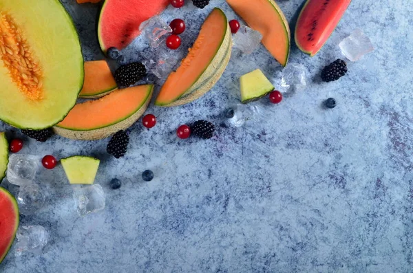Taze kesilmiş kavun, karpuz, böğürtlen ve buz küpleri mavi taştan arka planda. Boşluk ve metin alanını kopyala
