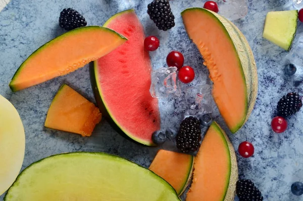 Taze kesilmiş kavun, karpuz, böğürtlen ve buz küpleri mavi taştan arka planda. Boşluk ve metin alanını kopyala