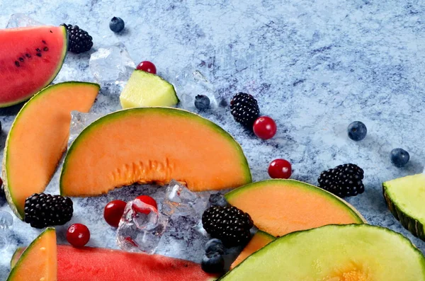 Taze kesilmiş kavun, karpuz, böğürtlen ve buz küpleri mavi taştan arka planda. Boşluk ve metin alanını kopyala