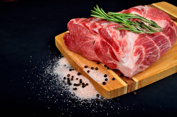 Tahtada taze domuz eti ve Himalaya tuzu, karabiber ve biberiye dalıyla süslenmiş siyah arka plan.
