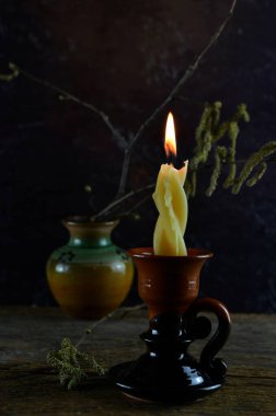 Çamur tutacağında yanan mum ve arka planda çiçek açan fındık dalı, koyu arkaplan