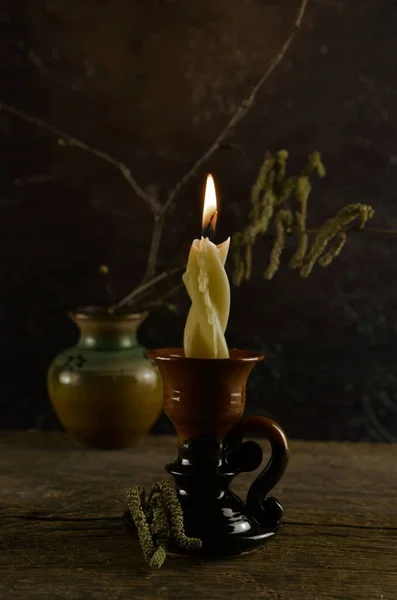 在粘土烛台上燃蜡蜡烛 在背景上开花的淡褐色枝干 深色背景 — 图库照片