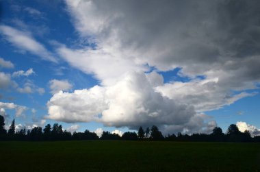 Yaz boyunca kara fırtına bulutları, Letonya 'nın ön planında ağaçlar ve çayırlar olan manzara. Düşük bulutlar