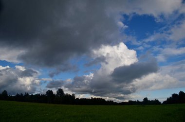 Yaz boyunca kara fırtına bulutları, Letonya 'nın ön planında ağaçlar ve çayırlar olan manzara. Düşük bulutlar