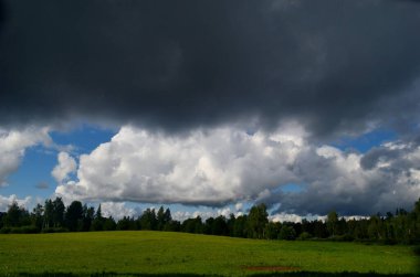 Yaz boyunca kara fırtına bulutları, Letonya 'nın ön planında ağaçlar ve çayırlar olan manzara. Düşük bulutlar