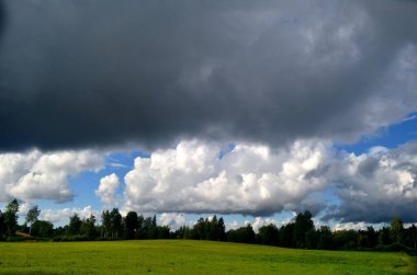 Yaz boyunca kara fırtına bulutları, Letonya 'nın ön planında ağaçlar ve çayırlar olan manzara. Düşük bulutlar