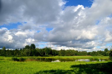 Yaz boyunca kara fırtına bulutları, Letonya 'nın ön planında ağaçlar ve çayırlar olan manzara. Düşük bulutlar