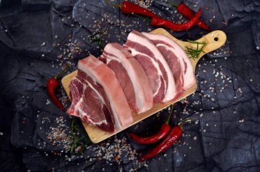 Baharatlı dilimlenmiş çiğ domuz bifteği ve siyah taş arka planda kırmızı biber. Üst görünüm