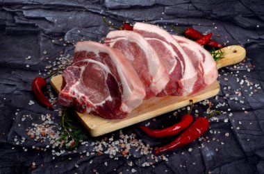 Baharatlı dilimlenmiş çiğ domuz bifteği ve siyah taş arka planda kırmızı biber. Üst görünüm