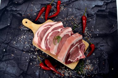 Baharatlı dilimlenmiş çiğ domuz bifteği ve siyah taş arka planda kırmızı biber. Üst görünüm
