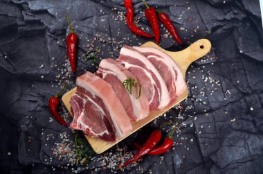 Baharatlı dilimlenmiş çiğ domuz bifteği ve siyah taş arka planda kırmızı biber. Üst görünüm