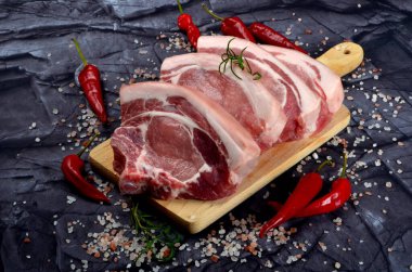 Baharatlı dilimlenmiş çiğ domuz bifteği ve siyah taş arka planda kırmızı biber. Üst görünüm
