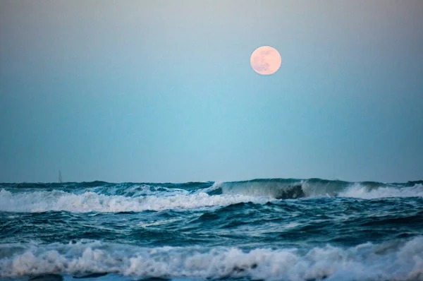 wild sea with full moon in background, focus on moon, blurry foreground