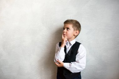 Okul üniformalı dalgın çocuk ilk kez okula gidiyor. Kapalı alanda hafif bir arka planda öğrenci. Harfleriniz için ücretsiz arkaplan hazır. Doğal duygular.