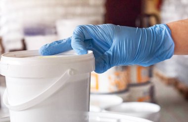 Mavi eldivenli bir adam elinde bir kutu boya tutuyor. Boya üretimi.