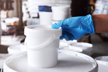 Mavi eldivenli bir adam elinde bir kutu boya tutuyor. Boya üretimi.