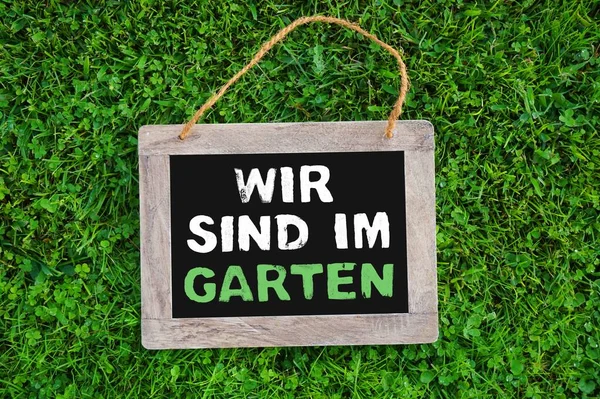 私たちは緑の草の木の黒板にドイツ語で庭にいます — ストック写真