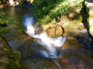 Güney Afrika 'nın orta kesimindeki Drakensberg' deki Cleos havuzuna akan şelalenin görüntüsü. Kayaların üzerinden akan suyun yumuşak fotoğrafı. Güneş ışığı ve kayaların üzerindeki yeşil bitki örtüsü..