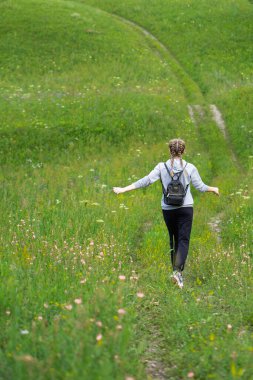 Mutlu genç kadın yeşil bir çayırda özgürlüğün tadını çıkarıyor. Doğada olmanın keyfi. Stres Rahatlama Konsepti. Yaz seyahati hafif. Etkin yaşam biçimi.