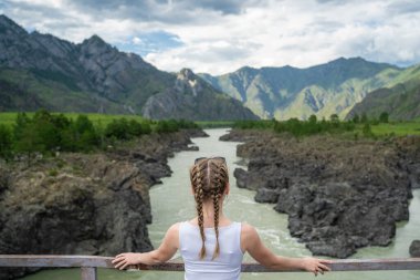 Bir dağ nehrinin üzerindeki köprüde duran genç bir kadın. Harika bir dağ manzarası. Şehirlerarası yolculuk. Doğayla baş başa mutluluk..