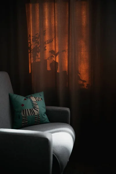 Cozy interior with an armchair and a pillow in the morning light through the curtains. Soft focus, beautiful shadows from home plants. Stay at home concept.