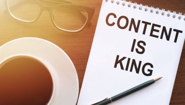 İçerik King - beyaz defter yazılı tahta masa üzerinde bir fincan kahve. Dijital İş Konsepti