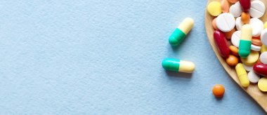 İlaç hapları, tabletler ve kapsüller mavi masadaki tahta kaşıkta. Tıbbi ve sağlık konsepti