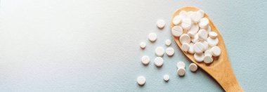 Beyaz haplar, mavi masadaki tahta kaşıkta tabletler. Tıp ve sağlık konsepti. Eczacılık. Üst Manzara. Haplar ve vitaminler.