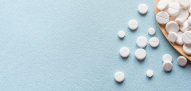 Beyaz haplar, mavi masadaki tahta kaşıkta tabletler. Tıp ve sağlık konsepti. Eczacılık. Üst Manzara. Haplar ve vitaminler.