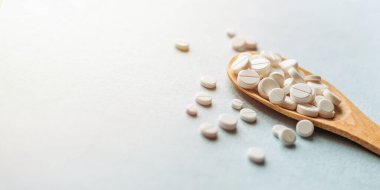 Beyaz haplar, mavi masadaki tahta kaşıkta tabletler. Tıp ve sağlık konsepti. Eczacılık. Haplar ve vitaminler.