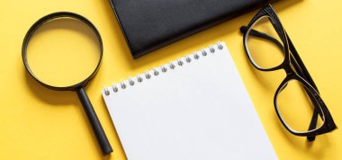 Sarı arka planda not defteri, büyüteç ve siyah gözlüklü iş konsepti