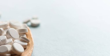 Beyaz haplar, mavi masadaki tahta kaşıkta tabletler. Tıp ve sağlık konsepti. Eczacılık. Haplar ve vitaminler.