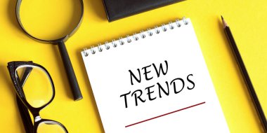 Not defterine gözlüklü yeni trend metni, sarı masadaki ucu büyüteç. Bir şeyleri değiştirmenin ana trendi. Popüler ve ilgili konular. İş hayatında yeni trendler. Yeni ve son moda. Değerlendirme yöntemleri.