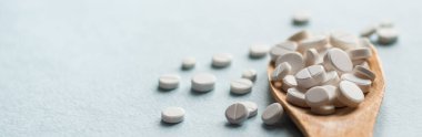 Beyaz haplar, mavi masadaki tahta kaşıkta tabletler. Tıp ve sağlık konsepti. Eczacılık. Haplar ve vitaminler.