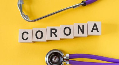 Sarı arka planda CORONA harfleri olan tahta bloklar, covid-19, koronavirüs, sağlık steteskopu. Salgın, tıbbi konsept