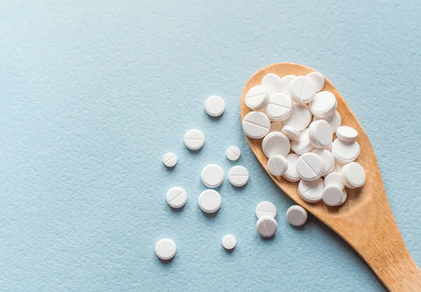 Beyaz haplar, mavi masadaki tahta kaşıkta tabletler. Tıp ve sağlık konsepti. Eczacılık. Üst Manzara. Haplar ve vitaminler.
